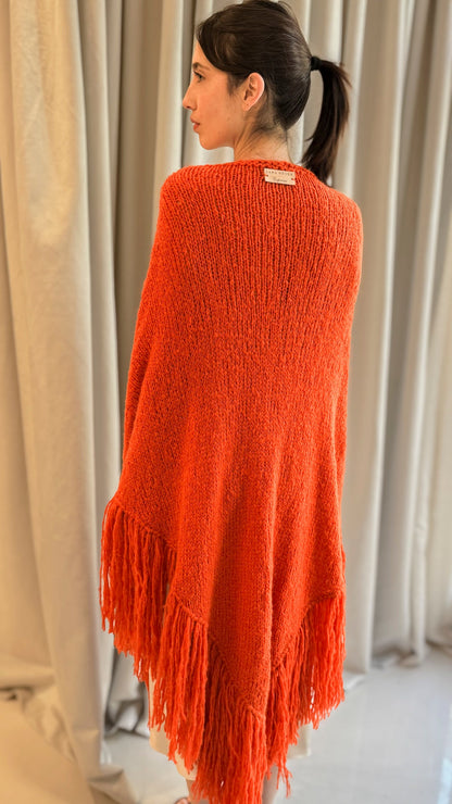 JUJUY THROW in Orange - Three-quarter back view on female model showing the bright woven drape and fringe